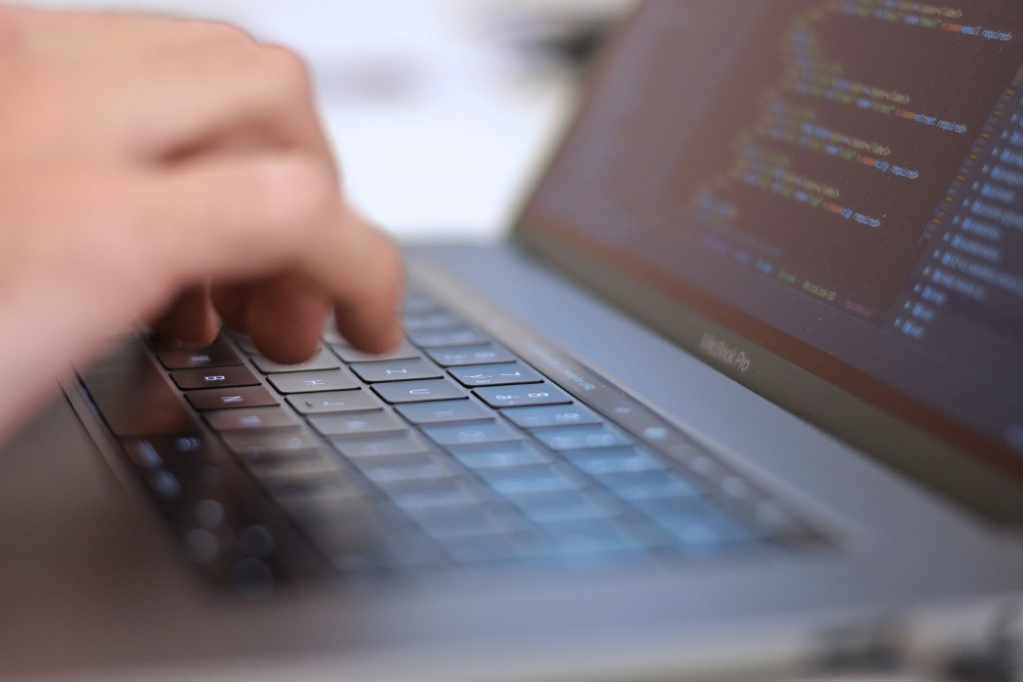 Dłonie piszące kod programistyczny na klawiaturze laptopa.